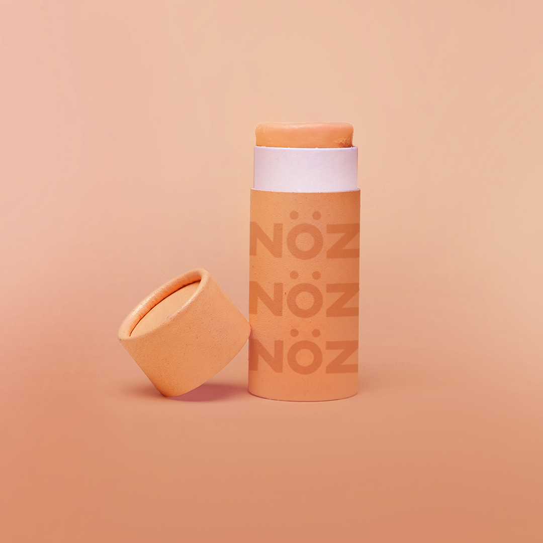 close up of the orange Noz face sunscreen stick with the cap off of it, all in front of a orange background