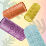 Load image into Gallery viewer, four face sunscreen sticks in the colors blue, yellow, orange, and purple sprawled out as if thrown in the air all in front of a yellow and pink background with watermark leaves on it
